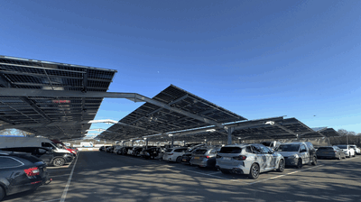 Overdekte parkeergelegenheid met zonnepanelen, vol met voertuigen onder een heldere blauwe lucht.