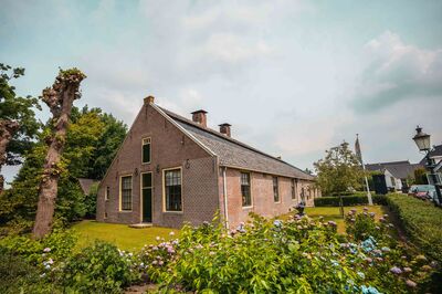 Traditioneel huis met een tuin, omringd door bomen en een kleurrijke bloeiende border.